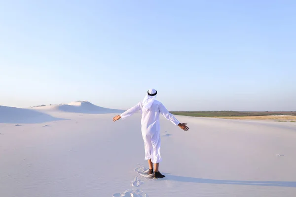 Zadowolony mężczyzna Emiraty spacery wzdłuż biały piasek pustyni i raduje się w ne — Zdjęcie stockowe
