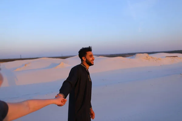 Молоді чоловіки мусульманської веде дівчина вручну і прогулянки по пустелі на с — стокове фото