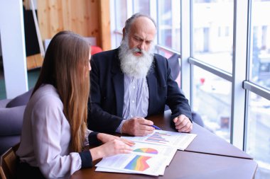 Yaşlı patron adam işaretleri belge raporları ile genç asistanı ile