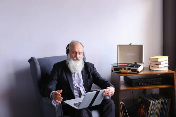 Senior werkt op computer en geniet van de muziek op de hoofdtelefoon via — Stockfoto
