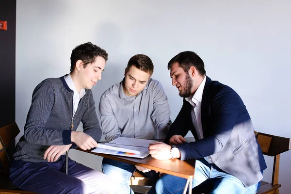 Trzech młodych mężczyzn programistów komunikować się za pomocą tabletu podczas sitt — Zdjęcie stockowe