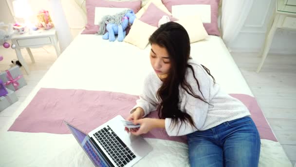 Симпатичная женщина ведет финансовый учет и использует ноутбук, сидя на кровати в яркой спальне с елкой . — стоковое видео