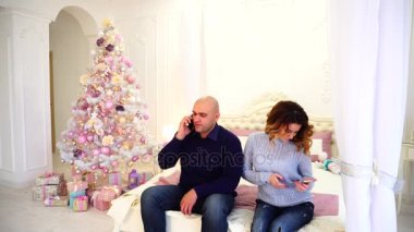 Mutlu karı koca yatak odası ve neşeli Noel ağacı yatakta oturup tatil günlerinde, yakınları tebrik için smartphone kullanın.