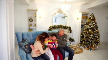 Mutlu ve neşeli şenlikli ruh var eğlenceli ve kahkaha birlikte, mavi kanepe Noel ağacı ile şenlikli bir şekilde dekore edilmiş oda ve şömine gündüz oturan.