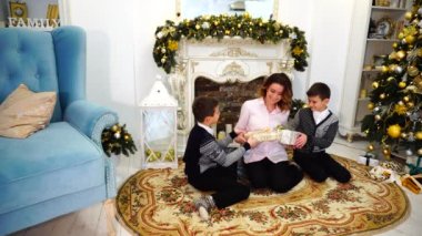 Güzel kadın ve yeni yıl hediye alışverişi ve oturma odasında şömine ve uzun ağaç ile tatil için dekore edilmiş katta oturan iki erkek çocuk bakım anne.