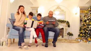 Ailesi gelişmiş, iki çocuk ve karı koca kendi iş için eğlence, aygıtları ile mavi kanepe ağaç şenlikli bir şekilde dekore edilmiş oda ve öğleden sonra şömine oturup nişanlandık