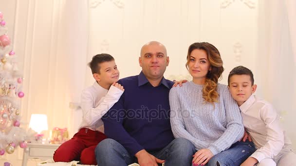 Hermoso retrato de la familia moderna y amorosa, dos hermanos gemelos y padres cariñosos están sentados en la cama en el dormitorio con árbol de Navidad festivo en el día de invierno . — Vídeos de Stock