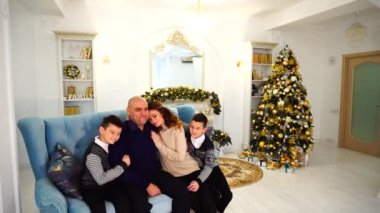 Portre sevimli ve örnek aile, bakım anne ve mavi Divan şenlikli oturan çocuk Noel ağacı ve şömine Oda dekore edilmiş gündüz.