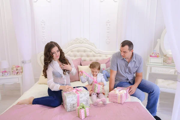 Família amigável no humor festivo para trocar presentes sentados na cama — Fotografia de Stock
