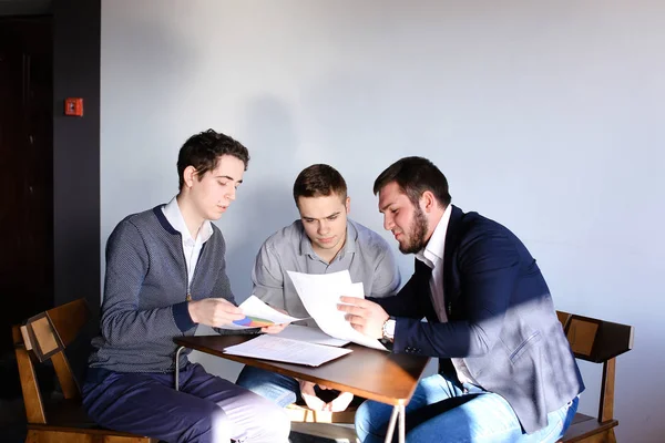 Tres jóvenes programadores masculinos se comunican usando tableta mientras están sentados — Foto de Stock