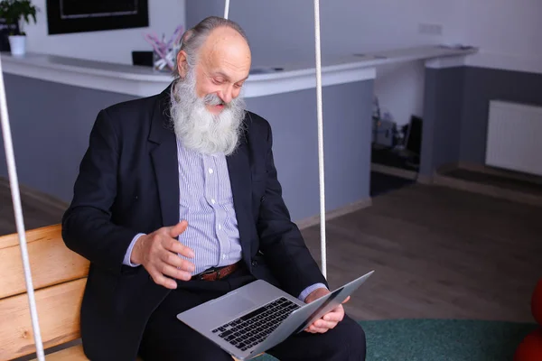 Oude gepensioneerde man maakt gebruik van de laptop en communiceert met collega's beh — Stockfoto