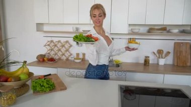Sevimli kız poz ve plaka salata ve patates kızartması gülümseme ile yüzünde, holding modern mutfağın ortasında duruyor.