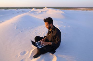Yakışıklı genç Arap dizüstü kullanarak Internet üzerinde yazıyor ve oturur