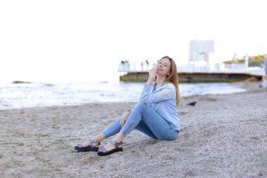 Gülümseyen genç kadın kumsalda aittir ve kamera, oturan pozlar
