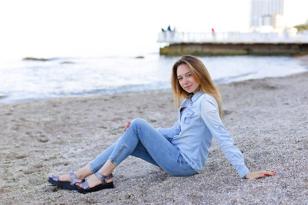 Gülümseyen genç kadın kumsalda aittir ve kamera, oturan pozlar