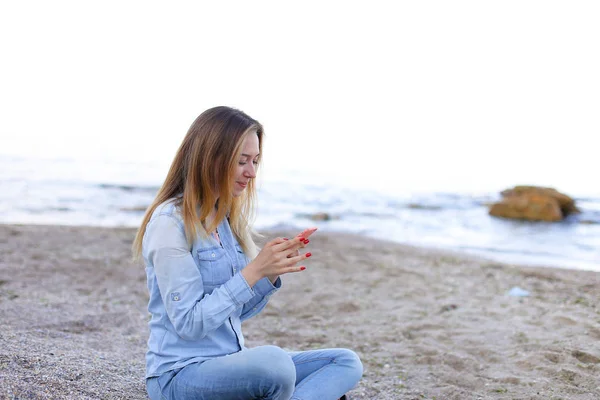 Hermosa chica charla por teléfono con sonrisa y se sienta en la playa n — Foto de Stock