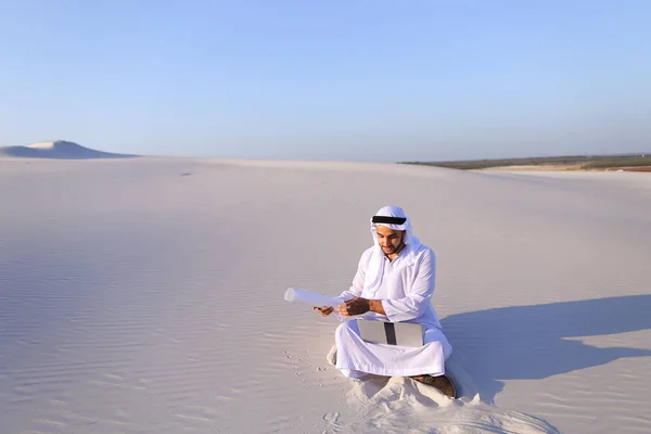 สถาปนิกชายมุสลิมนั่งกับแล็ปท็อปบนทรายในทะเลทรายบน h — ภาพถ่ายสต็อก