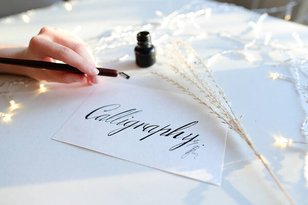 Female master of lettering of ink writes word on paper, sitting