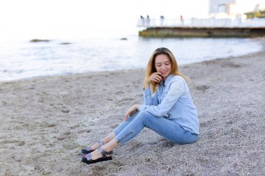 Gülümseyen genç kadın kumsalda aittir ve kamera, oturan pozlar