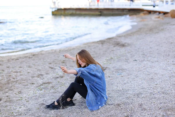 Gülümseyen genç kadın kumsalda aittir ve kamera, oturan pozlar