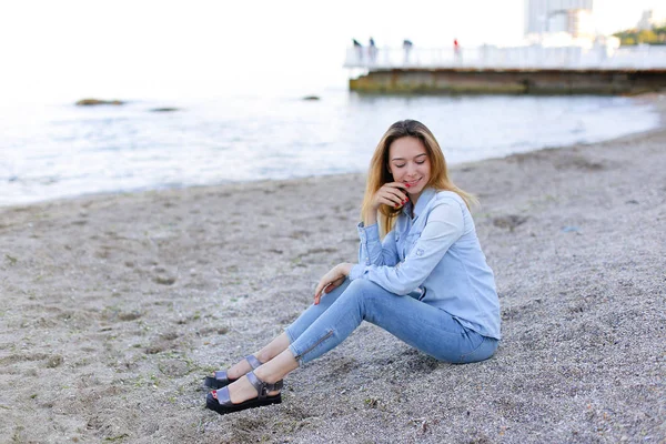 Gülümseyen genç kadın kumsalda aittir ve kamera, oturan pozlar — Stok fotoğraf