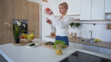 Akıllı kız dilim salatalık ile bıçak ve gülümsüyor, şık mutfak mutfak masasında duran.