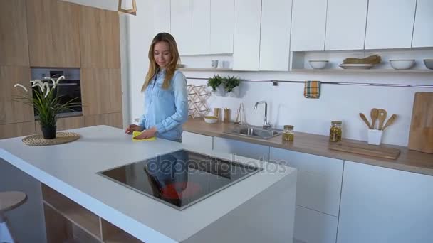 Nice bela dona de casa feminina limpa a superfície da cozinha em pé no meio da cozinha moderna no quarto durante o dia . — Vídeo de Stock