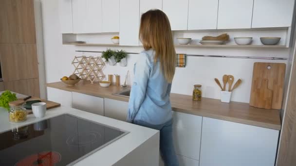 Donna attraente entra in cucina e gode di caffè tonificante, in piedi in mezzo alla cucina al tavolo della cucina al mattino . — Video Stock