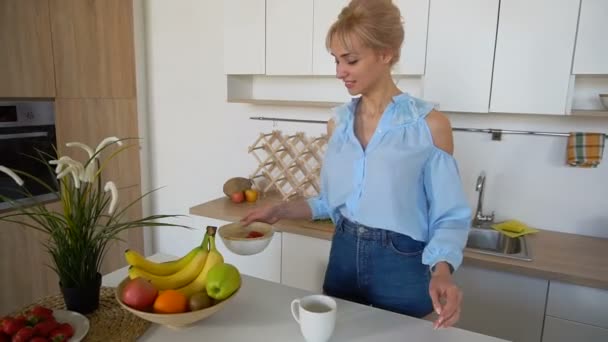 Adorabile ragazza felice con l'inizio del nuovo giorno e si prepara domani mattina, in piedi in mezzo alla cucina al tavolo della cucina al mattino . — Video Stock