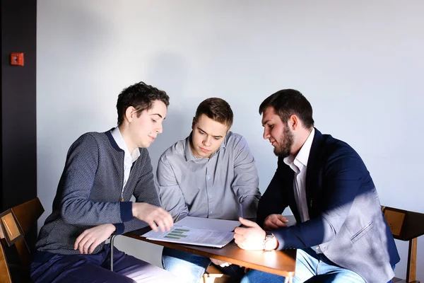 Três jovens programadores do sexo masculino se comunicam usando tablet enquanto sentam — Fotografia de Stock