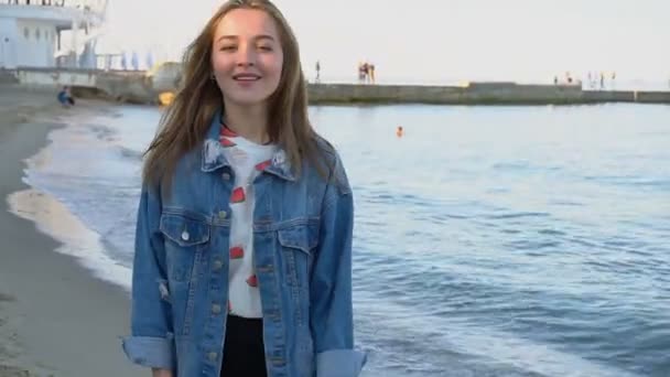 Stilvolle Frau in Zeitlupe schreitet selbstbewusst am Strand entlang und posiert an einem sonnigen Sommerabend mit einem Lächeln in der Kamera. — Stockvideo