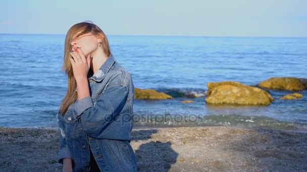 Любимая девушка вышла на берег Черного моря, улыбаясь и отводя взгляд, стоя на пляже в прохладный летний день . — стоковое видео