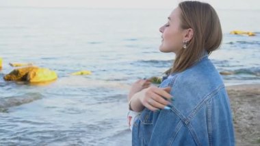 Ağır çekim portre sevimli kadın taze deniz havası ve pozlar ile nefes gülümseme, mavi deniz ve gökyüzü karşı akşamları duruyor.