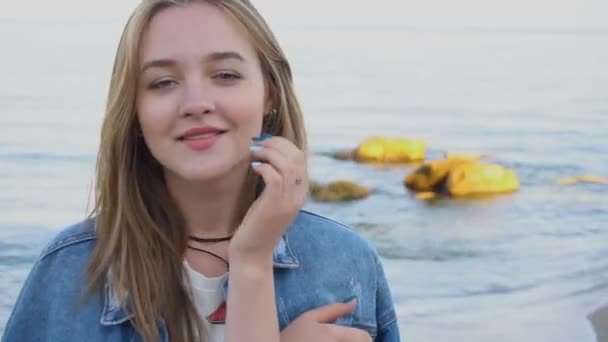 Portrait de tendre fille qui pose à la caméra, mignon sourire et se tient contre la mer bleue et le ciel au coucher du soleil en été . — Video