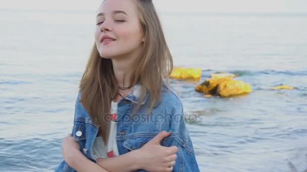 Slow Motion porträtt av söt flicka poserar och ler mot kameran, stående av havet på varm sommarkväll. — Stockvideo