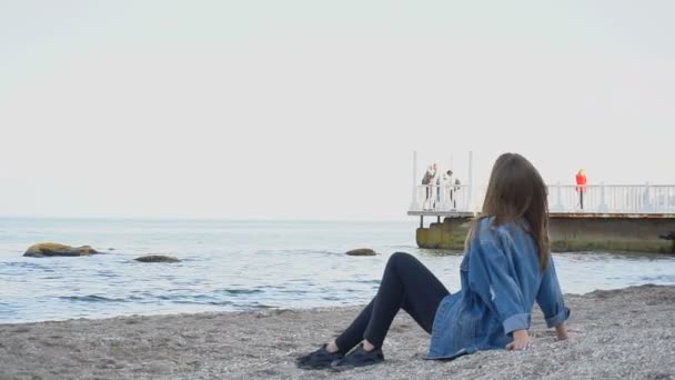 Slow Motion doordachte vrouw kijkt zeegezicht en luistert naar surfen, zittend op een zandstrand op warme avond. — Stockvideo