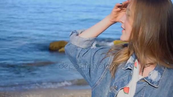 Slow Motion Happy young woman looking into distance and turning with smile on face to camera, standing on background of sea water. — Stock Video