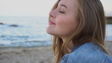 Yaz aylarında gün batımında kum mavi deniz ve gökyüzü arka plan üzerinde oturan ağır çekim portre fotoğraf makinesinde ve sevimli pozlar neşeli kız güler.