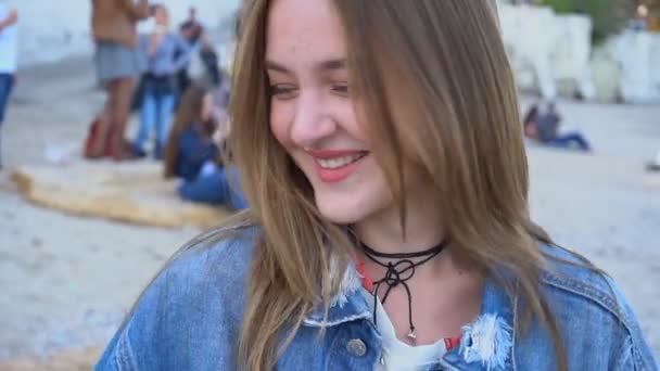 Gros plan portrait de fille mignonne qui sourit timide et posant à la caméra, debout sur la plage le soir chaud de printemps . — Video