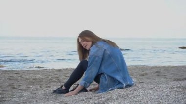 Gülümseyen genç kadın yalnız deniz kenarında oturan rahatlatır ve öğleden sonra kabukları ile kum plajındaki çevresinde doğa hayran.