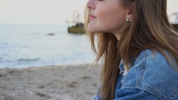 Porträt eines schönen Mädchens, das salzige Meeresluft atmet, sitzt am Strand von Sandstrand an einem kühlen Sommerabend. — Stockvideo