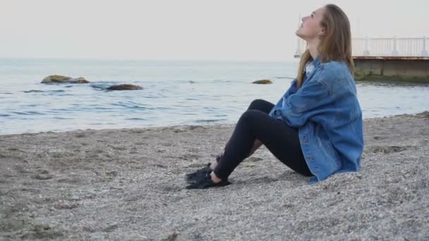 Slow Motion Charming girl enjoys holiday in sea city and half asleep on beach against backdrop of sea and sky on warm summer evening — Stock Video