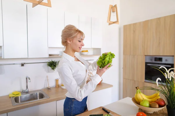 Beautiful housewife woman holding green lettuce leaf and smiling