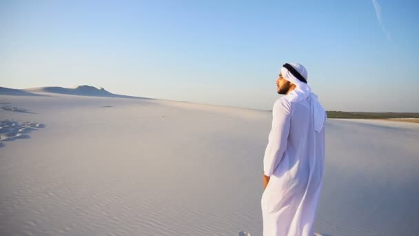 Slowmotion bewegingen van Arabische Uae Sheikh man naar top van zandstrand heuvel over witte zand in de woestijn op een heldere dag. — Stockvideo