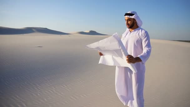 Wise moslim Arabische Uae Sheikh bouw guy inspecteert gebied en leest blauwdruk voor bouw, staande in het midden van de woestijn op warme dag. — Stockvideo