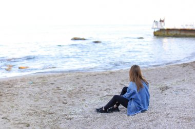 Gülümseyen genç kadın kumsalda aittir ve kamera, oturan pozlar