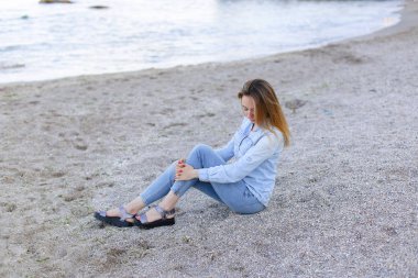 Gülümseyen genç kadın kumsalda aittir ve kamera, oturan pozlar