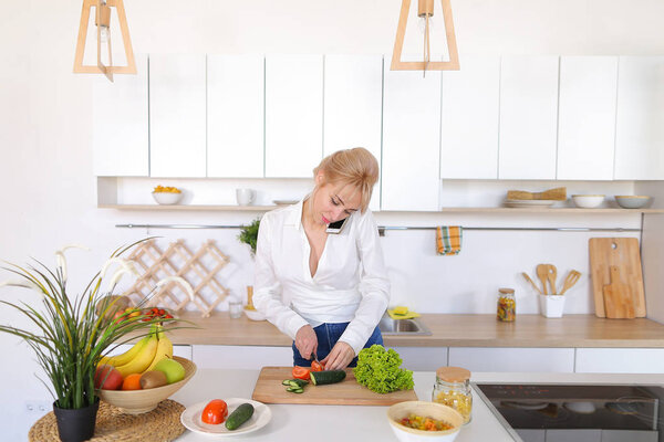 Симпатичная домохозяйка болтает по сотовому и улыбается, готовит сал
