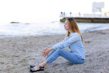 Gülümseyen genç kadın kumsalda aittir ve kamera, oturan pozlar