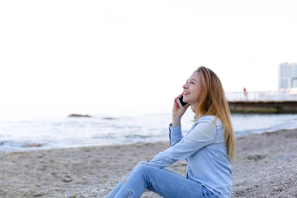 Mulher bonita fala no celular com sorriso e senta-se na praia n — Fotografia de Stock